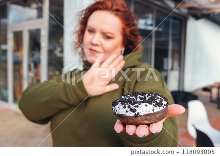 A blurry portrait of a well-fed woman holding a chocolate donut in the palm of her hand. The concept of diet and weight loss A blurry portrait of a well-fed woman holding a chocolate donut in the palm of her hand. The concept of diet and weight loss 118093008