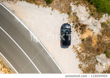 Top view of black car with a roof box, parked beside a coastal road on a steep cliff Top view of black car with a roof box, parked beside a coastal road on a steep cliff 118094404