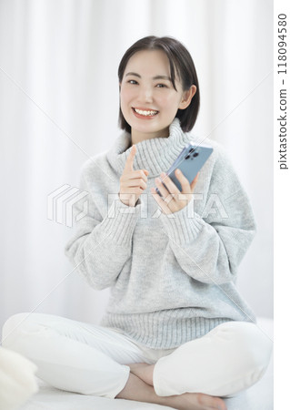 A young woman wearing a sweater using a smartphone 118094580