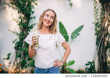 Woman enjoys a refreshing drink in a lush garden during a sunny afternoon Woman enjoys a refreshing drink in a lush garden during a sunny afternoon 118094984