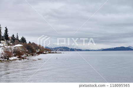 Scenic view of city buildings and a winter lake with snow-capped mountains in the background Scenic view of city buildings and a winter lake with snow-capped mountains in the background 118095565