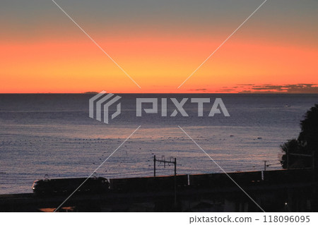 A freight train runs through the night with the orange sky and blue sea before sunrise in the background. 118096095