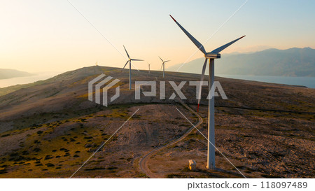 Wind turbines generate eco-friendly power on Pag Island, encircled by the Adriatic Sea at sunset.  118097489