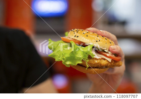 Hands holding a hamburger sprinkled with sesame seeds on a blurred background. Hands holding a hamburger sprinkled with sesame seeds on a blurred background. 118097707