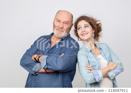 An adult daughter with an elderly father in denim clothes posing and looking at the camera. Daughter-in-law and father-in-law on a gray background. An adult daughter with an elderly father in denim clothes posing and looking at the camera. Daughter-in-law and father-in-law on a gray background. 118097911