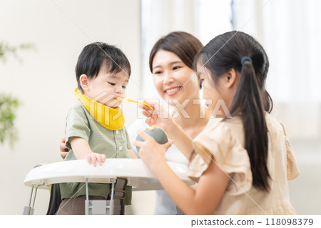An older sister feeding her 0-year-old brother baby food 118098379
