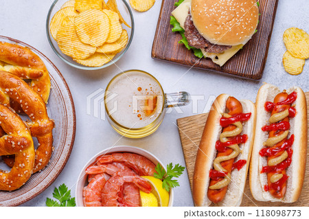 A vibrant photo showcasing a glass of beer surrounded by various snacks and fast food A vibrant photo showcasing a glass of beer surrounded by various snacks and fast food 118098773