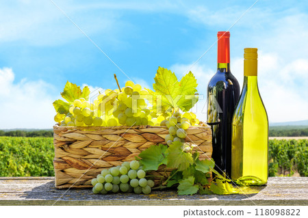 A basket filled with various types of grapes and bottles of red and white wine 118098822