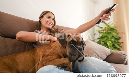 Happy woman with Boxer dog watching TV in modern home 118098977