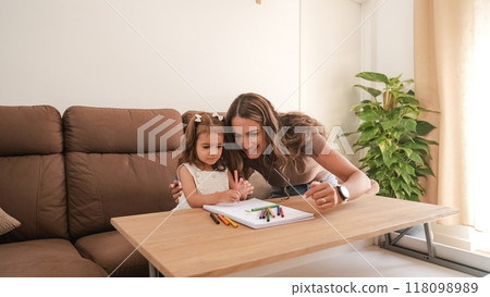 Caring mother and daughter drawing in book at apartment Caring mother and daughter drawing in book at apartment 118098989