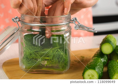 Woman putting cucumbers in glass jar to cook pickles on kitchen, hands close-up. Woman putting cucumbers in glass jar to cook pickles on kitchen, hands close-up. 118099649