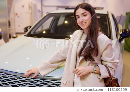 Portrait of successful smiling woman in fashionable beige suit looking at camera and posing next to newly bought car at dealership center, copy space Portrait of successful smiling woman in fashionable beige suit looking at camera and posing next to newly bought car at dealership center, copy space 118100209