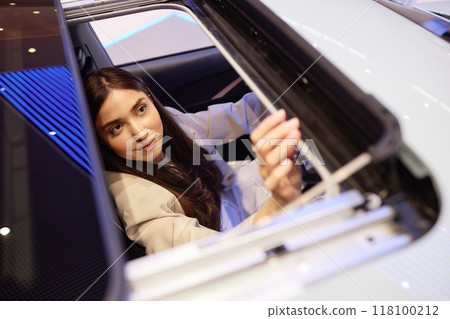 Shot through opened car sunroof of young woman inspecting interior details of demo vehicle while deciding on specific model at dealership center, copy space 118100212