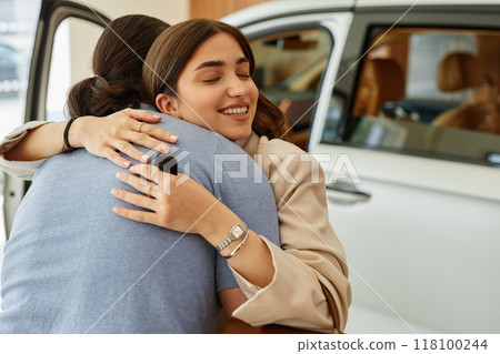 Medium shot of happy young woman embracing boyfriend after successful car buying at dealership center, copy space Medium shot of happy young woman embracing boyfriend after successful car buying at dealership center, copy space 118100244