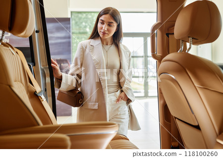 Shot from car cabin with beige leather interior of pensive fashionable woman examining passenger compartment deciding on buying new vehicle at dealership center Shot from car cabin with beige leather interior of pensive fashionable woman examining passenger compartment deciding on buying new vehicle at dealership center 118100260