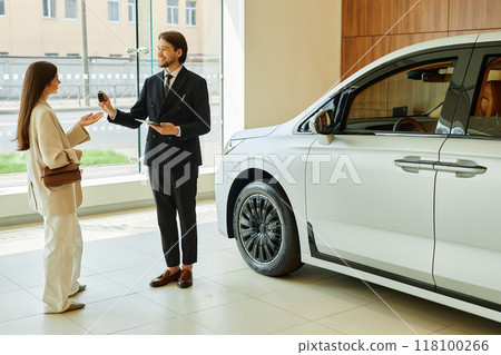 Full shot of smiling auto dealer handing key of new vehicle to female customer after successful car buying next to new automobile at dealership center Full shot of smiling auto dealer handing key of new vehicle to female customer after successful car buying next to new automobile at dealership center 118100266