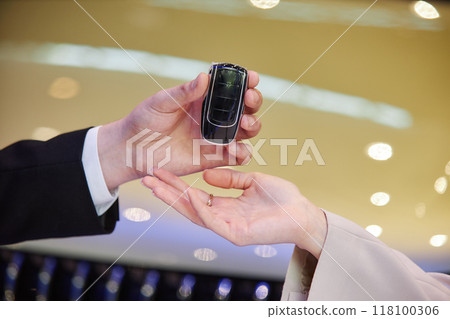 Close up on male auto dealers hand giving smart key of new vehicle to female buyer at car dealership center, copy space Close up on male auto dealers hand giving smart key of new vehicle to female buyer at car dealership center, copy space 118100306