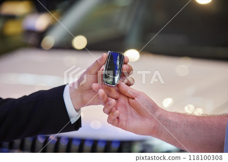 Close up on auto dealers hand giving smart key of new vehicle to male buyer at car dealership center, copy space 118100308
