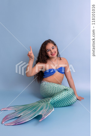A happy pretty girl in a mermaid costume sits on a blue background 118101016