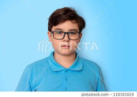 Portrait of a calm dark-haired boy with glasses on a light blue background, looking into the camera Portrait of a calm dark-haired boy with glasses on a light blue background, looking into the camera 118101029