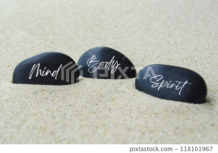 Mind, Body and Spirit text on black zen stones buried in the sand. Mind, Body and Spirit text on black zen stones buried in the sand. 118101967