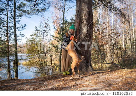 Woman hugging cuddling petting her dog walking on ecotrope in nature autumn park near pond. 118102885