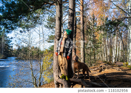Relaxed, meditative woman and dog enjoy peaceful walk by frozen lake, savoring crisp autumn weather Relaxed, meditative woman and dog enjoy peaceful walk by frozen lake, savoring crisp autumn weather 118102956