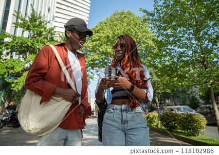 Stylish african american couple talking outdoor, stop walking on sidewalk looks at screen smartphone 118102986