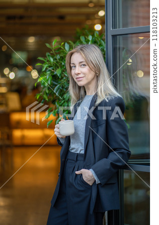 Smiling confident businesswoman drinks coffee during break, facing camera at cafe entrance outdoors Smiling confident businesswoman drinks coffee during break, facing camera at cafe entrance outdoors 118103213