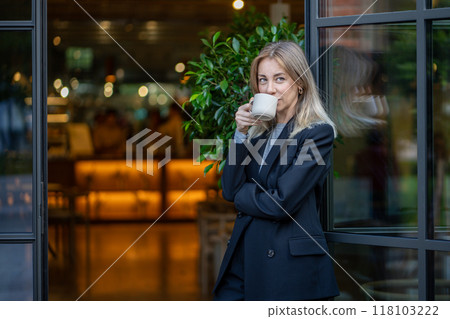 Confident pleased middle aged businesswoman drinks morning coffee standing at entrance of coffeeshop 118103222