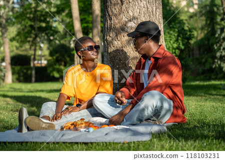 Happy black couple in love spend time together sits on grass in park chatting, looking to each other Happy black couple in love spend time together sits on grass in park chatting, looking to each other 118103231