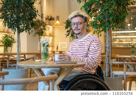 Alone thoughtful disabled young man on wheelchair spending time in cafe drinking coffee reflects. Alone thoughtful disabled young man on wheelchair spending time in cafe drinking coffee reflects. 118103256