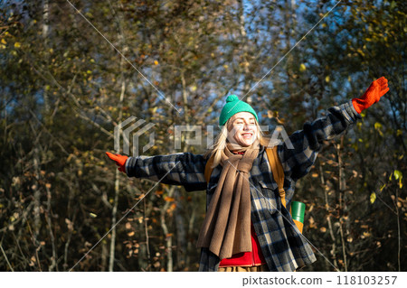 Carefree shiny woman with backpack spinnes with arms outstretched in fall forest. Adventure lover 118103257