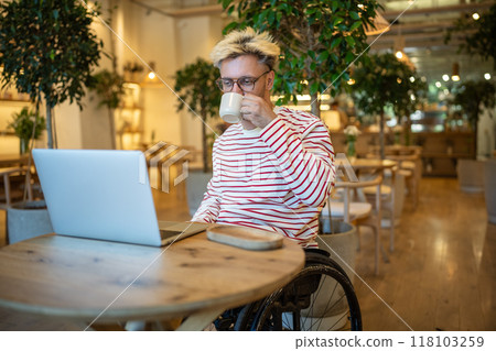 Interested man with disability drinking coffee in cafe freelance working online, watching on laptop. Interested man with disability drinking coffee in cafe freelance working online, watching on laptop. 118103259