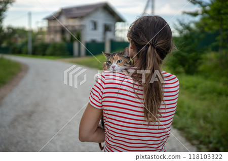 Rearview woman carrying scared tabby cat on shoulder, strolls through rural nature with domestic pet Rearview woman carrying scared tabby cat on shoulder, strolls through rural nature with domestic pet 118103322