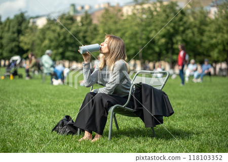 Relaxed woman drinking water from bottle relaxing in park on lawn sitting on folding chair. Relaxed woman drinking water from bottle relaxing in park on lawn sitting on folding chair. 118103352