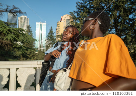 Glad African American girls spend time together on walk, communicate discuss various rumours in city Glad African American girls spend time together on walk, communicate discuss various rumours in city 118103391