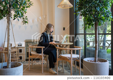 Thoughtful woman in business suit calling on phone sits with laptop in cafe pensive looks to window Thoughtful woman in business suit calling on phone sits with laptop in cafe pensive looks to window 118103400