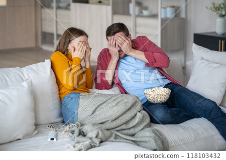 Scared family couple cover eyes with palms watching horrifying movie series sitting on couch at home Scared family couple cover eyes with palms watching horrifying movie series sitting on couch at home 118103432