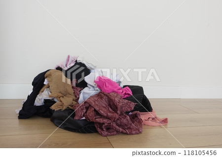 There is a disordered pile of mixed laundry scattered on a wooden floor against a plain wall There is a disordered pile of mixed laundry scattered on a wooden floor against a plain wall 118105456