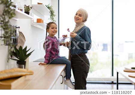 Muslim mother and daughter eating healthy salad together in kitchen 118110207