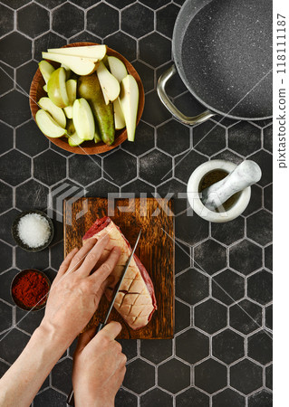 Chef slices criss-cross a piece of duck breast fat on a rustic wooden cutting board 118111187