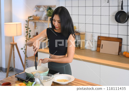 Smiling millennial woman in sportswear preparing meal in kitchen with fresh ingredients Smiling millennial woman in sportswear preparing meal in kitchen with fresh ingredients 118111435