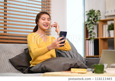 Happy young woman making video call on smartphone sitting on couch at home 118111465