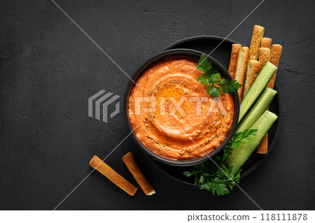 Htipiti - Greek red pepper and feta dip in black bowl with bread sticks and cucumbers, on dark background. top view, copy space Htipiti - Greek red pepper and feta dip in black bowl with bread sticks and cucumbers, on dark background. top view, copy space 118111878