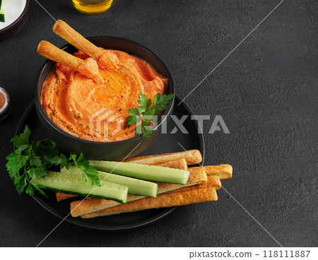 Greek feta spread Htipiti. Roasted red pepper, olive oil and feta dip served with sliced veggies and breadsticks, copy space, dark background 118111887