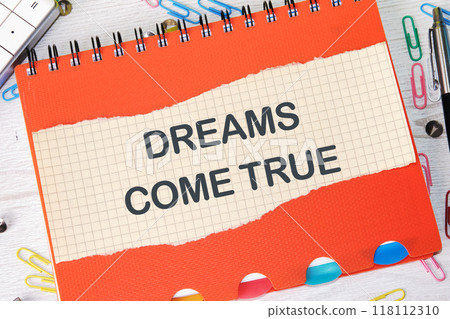Conceptual dreams come true symbol. Copy space. Dreams come true words on a piece of paper in a cage on the background of a notebook 118112310