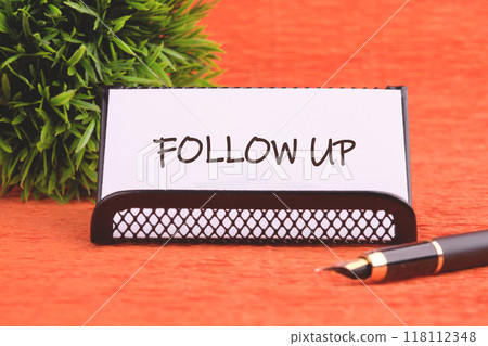 Business concept. Copy space. The words Follow Up on a white business card in a business stand in front of an orange background 118112348