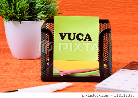 Volatility Uncertainty Complexity Ambiguity. VUCA text on a yellow sticker in a black stand on an orange background Volatility Uncertainty Complexity Ambiguity. VUCA text on a yellow sticker in a black stand on an orange background 118112355