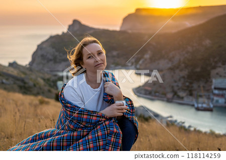 A woman is sitting on a hill with a blanket wrapped around her 118114259